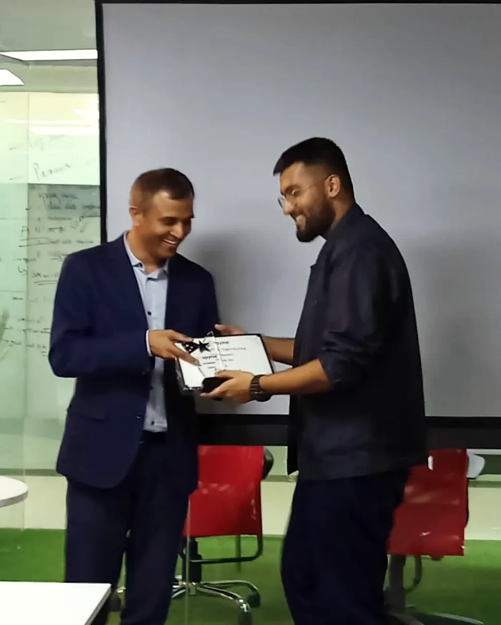 Anurag receiving a framed certificate from a colleague in an office.