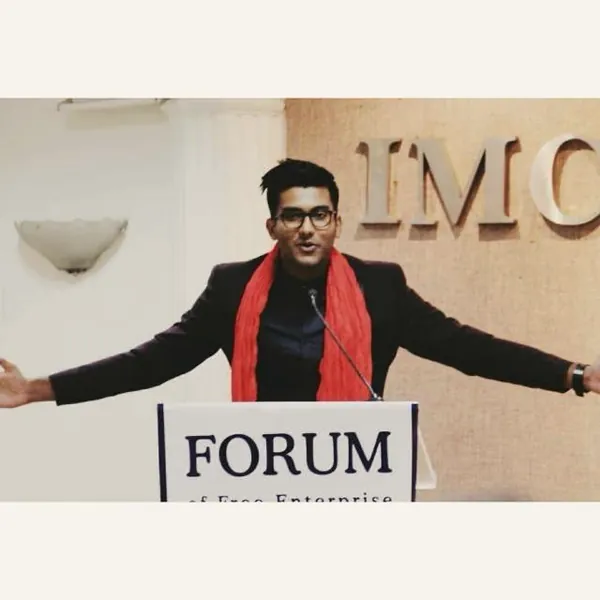 Anurag speaking with arms wide at a lectern at the Forum of Free Enterprise.