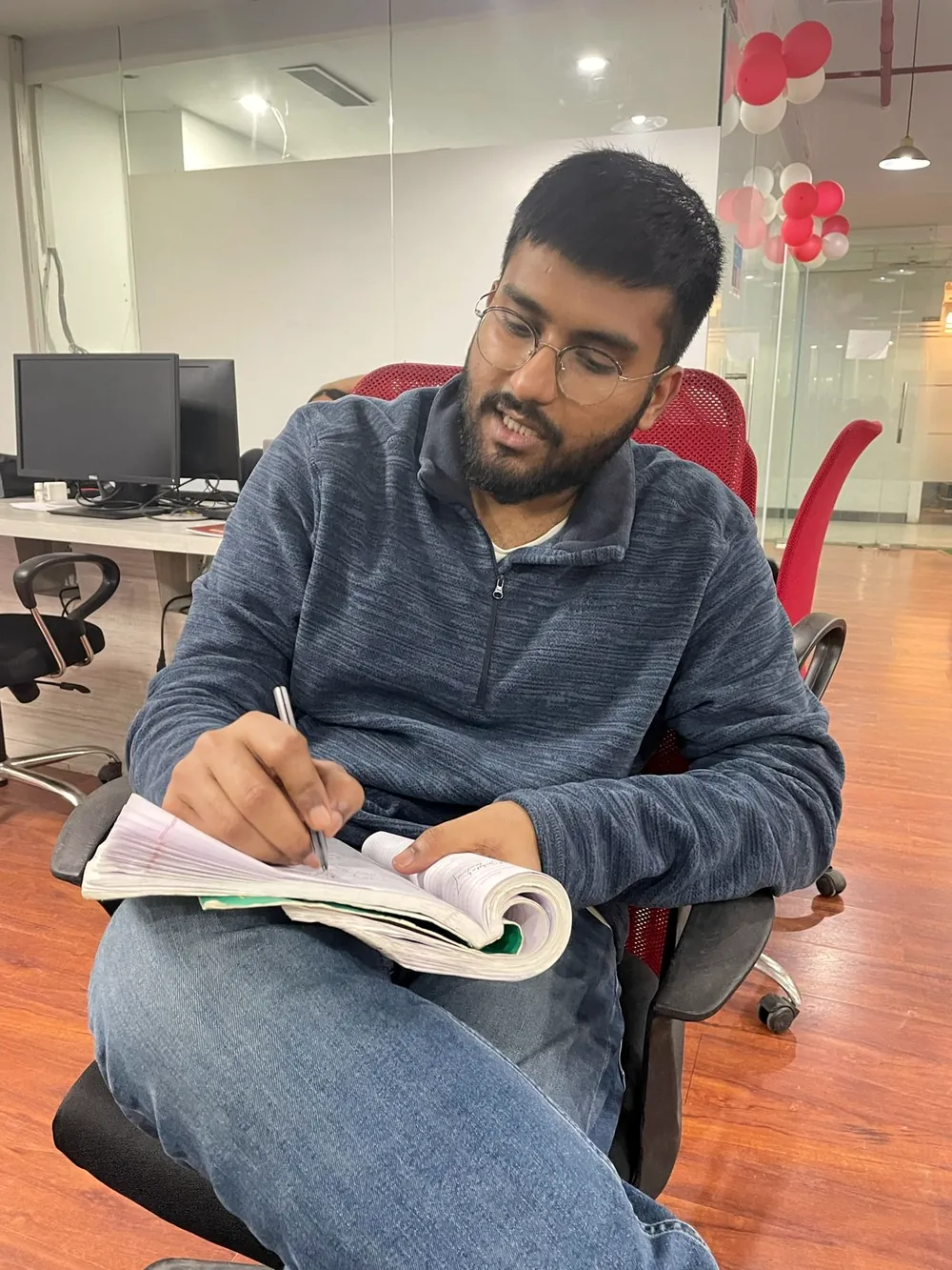 Anurag in an office chair writing in a notebook.