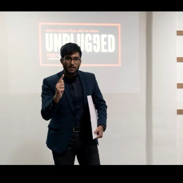 Anurag on stage holding a microphone in front of a screen reading Unplugged.